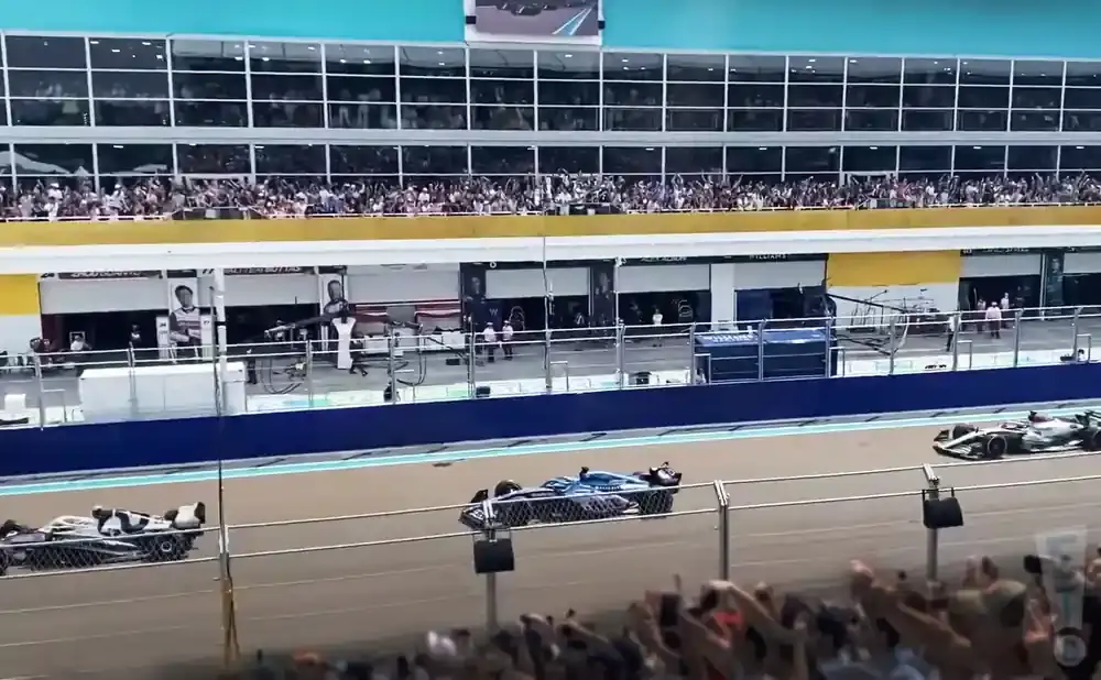A race car speeds past a pit stop with spectators in the grandstands.
