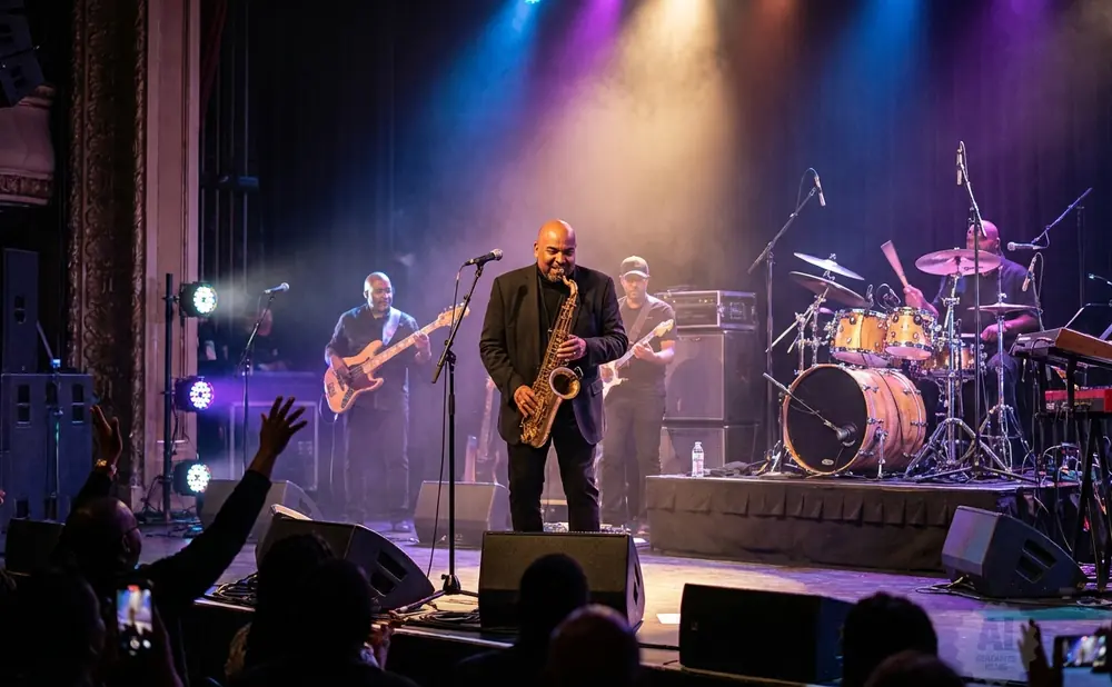 A band performs jazz music on a brightly lit stage, with a saxophonist in the foreground.