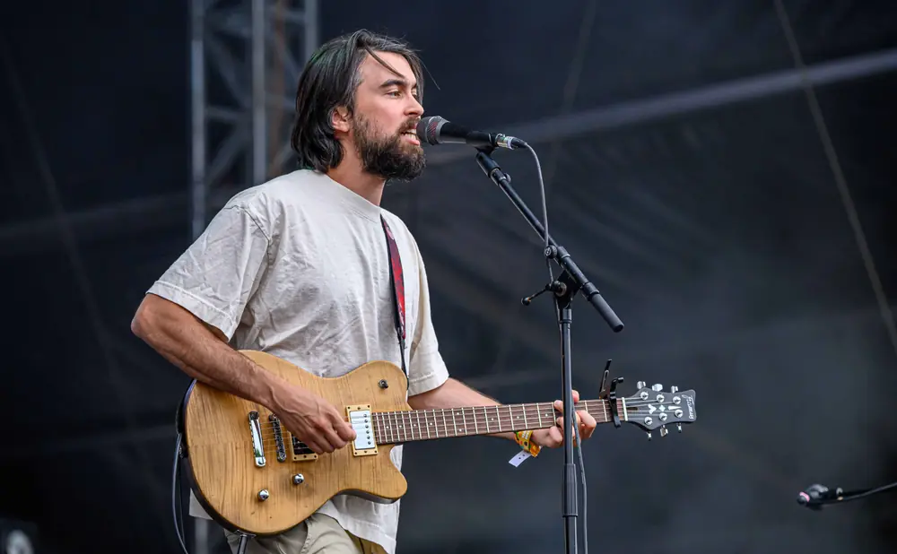 A man with a beard and long hair plays an electric guitar and sings into a microphone on stage.