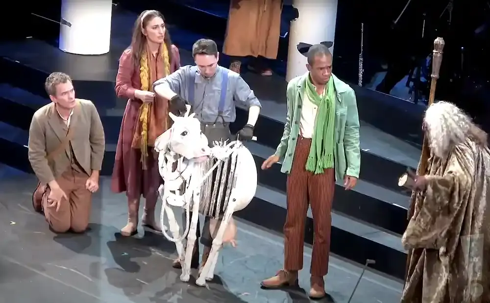 A stage scene with actors and a skeleton cow puppet.