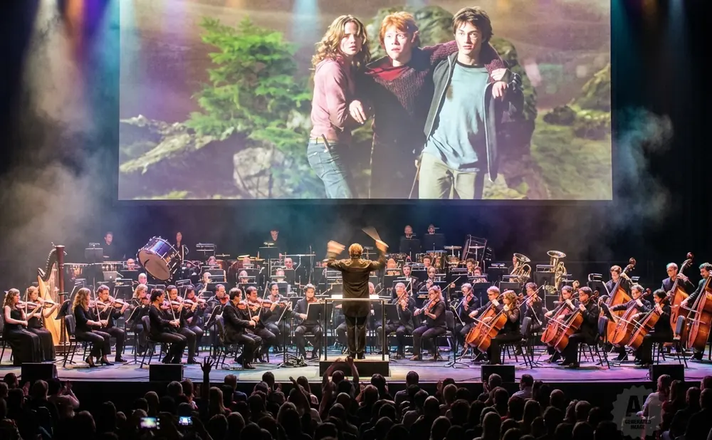 An orchestra plays in front of a screen showing Harry Potter characters Hermione, Ron, and Harry.