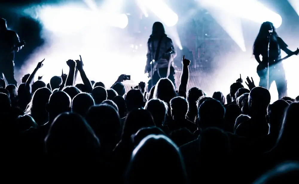 A silhouetted crowd at a concert, with bright stage lights illuminating the performers.