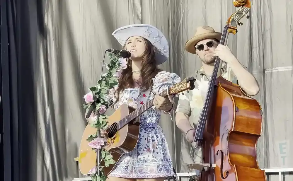 Singer with a star-spangled cowboy hat sings and plays guitar, accompanied by a man playing a double bass.