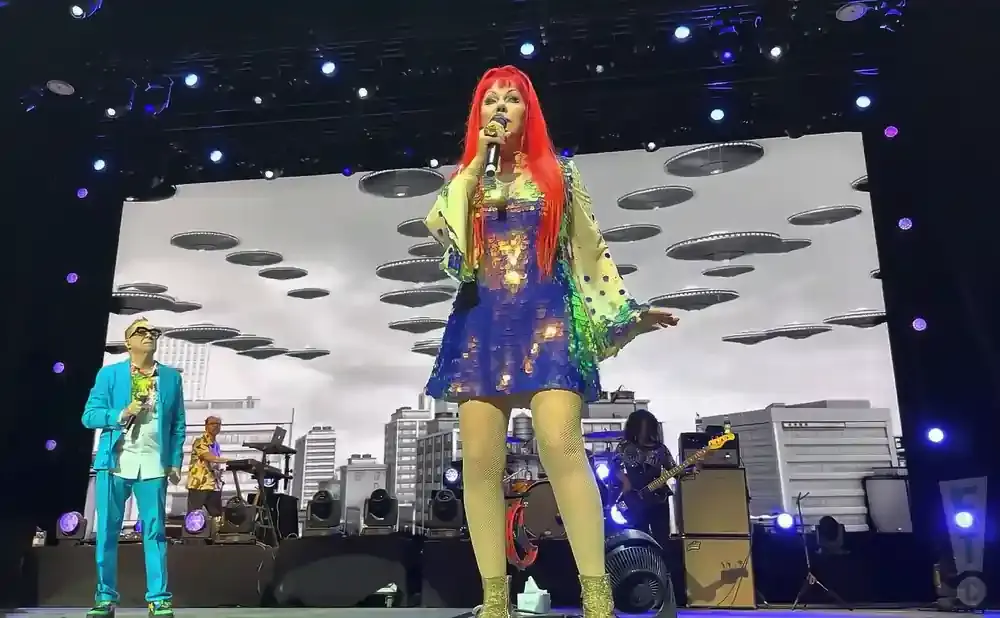 A singer with bright red hair performs on stage in a sequined blue dress.