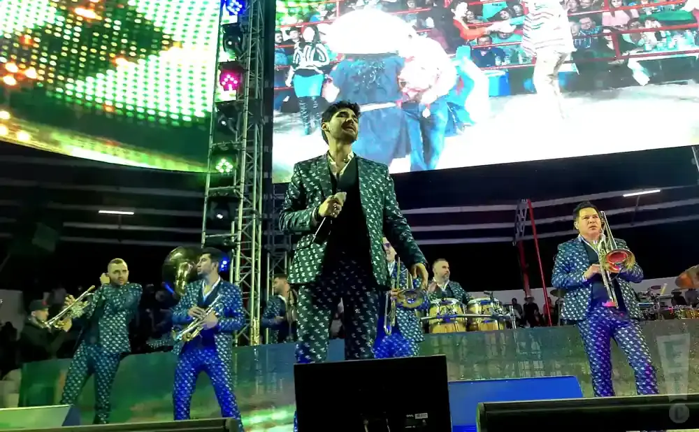 A band in matching sparkly suits performs on stage with a large screen behind them.
