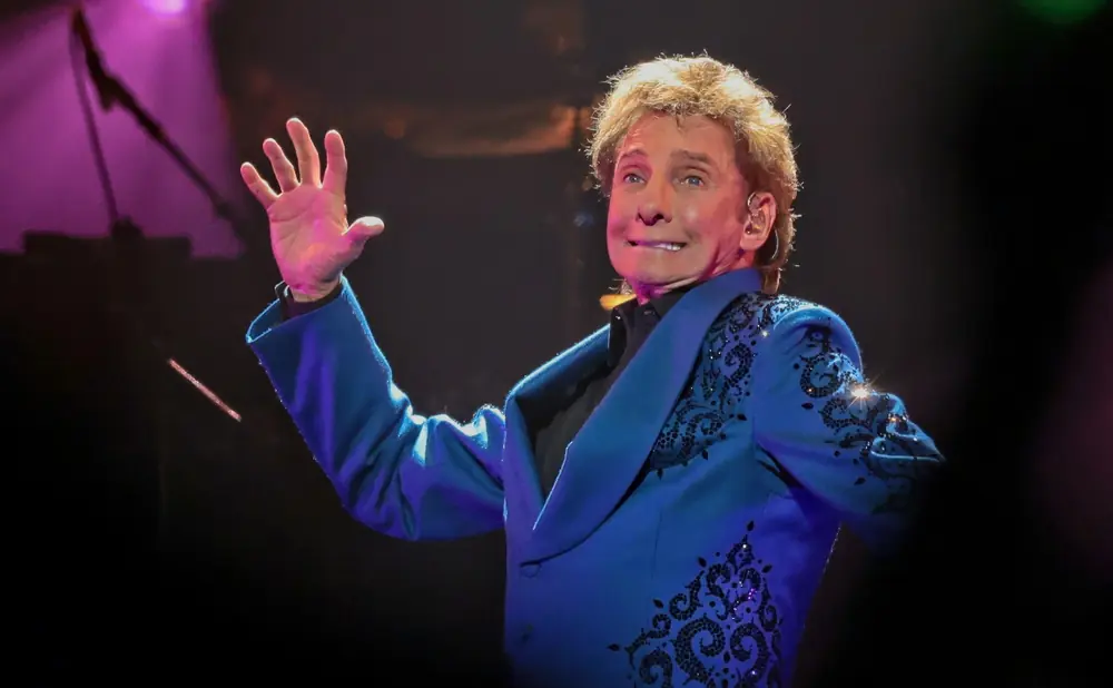 Singer Barry Manilow waves to the audience in a blue sequined jacket.