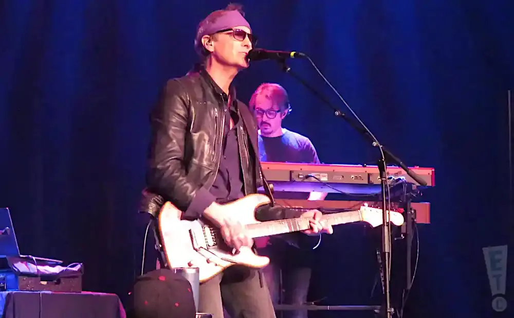 A guitarist sings into a microphone while another musician plays keyboards behind him.