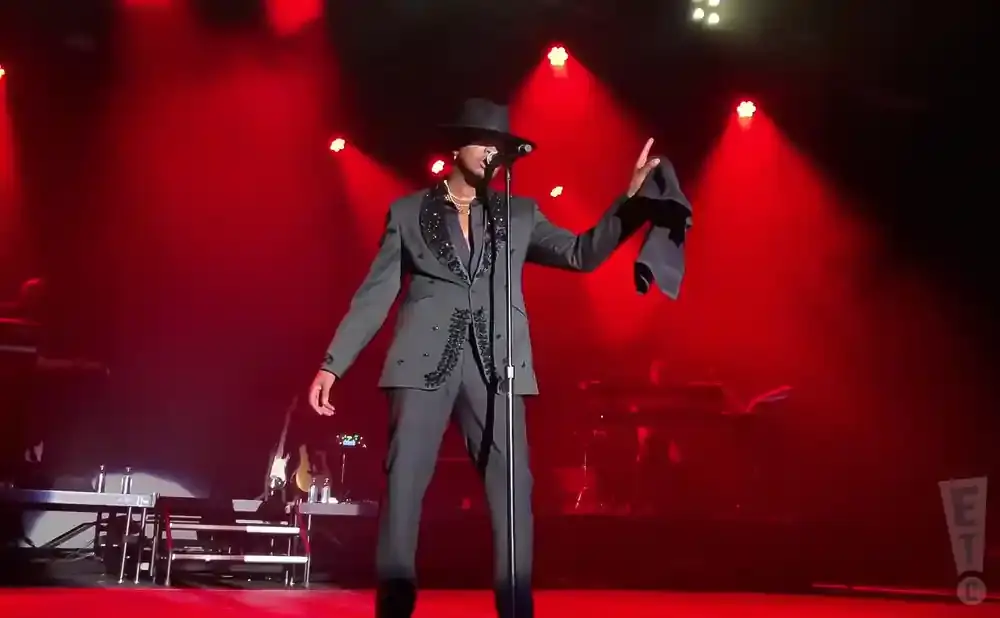 Singer in a black fedora and embellished suit performing on a red-lit stage, holding a dark cloth.