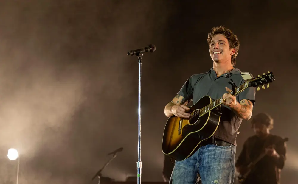 A man smiles and plays an acoustic guitar on stage.
