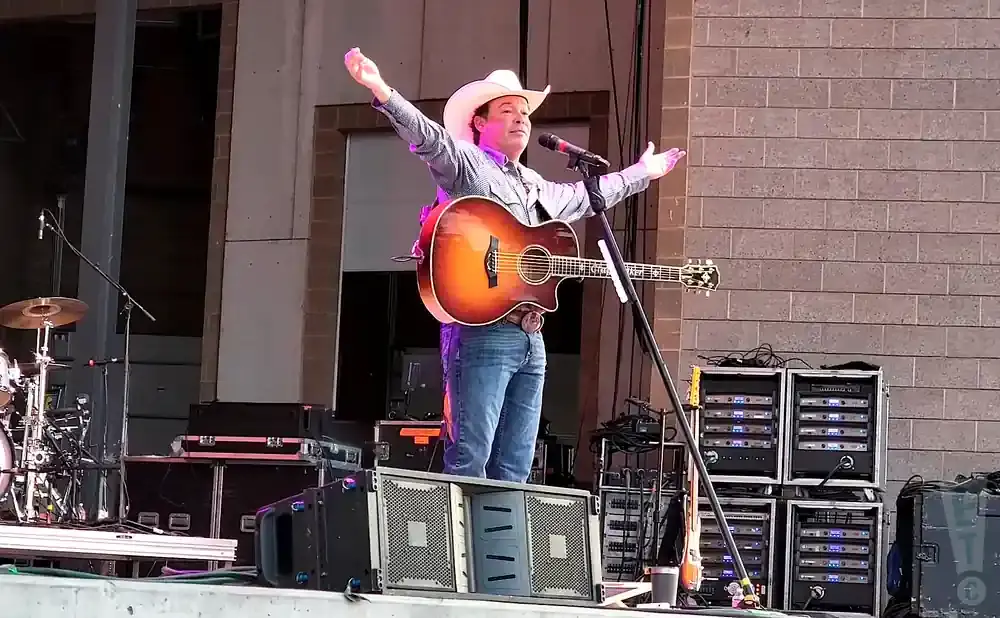 A country singer in a white cowboy hat performs with a guitar on stage.