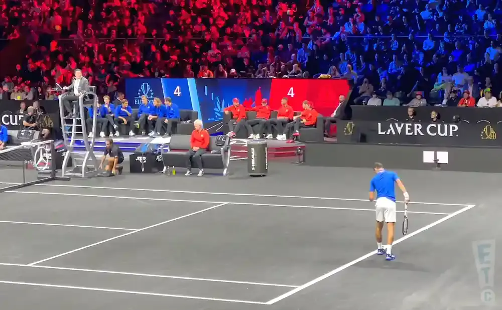 Tennis player in blue on court, with spectators in red and blue in the background.