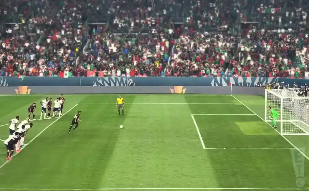 Soccer players line up for a free kick in a stadium filled with cheering fans.