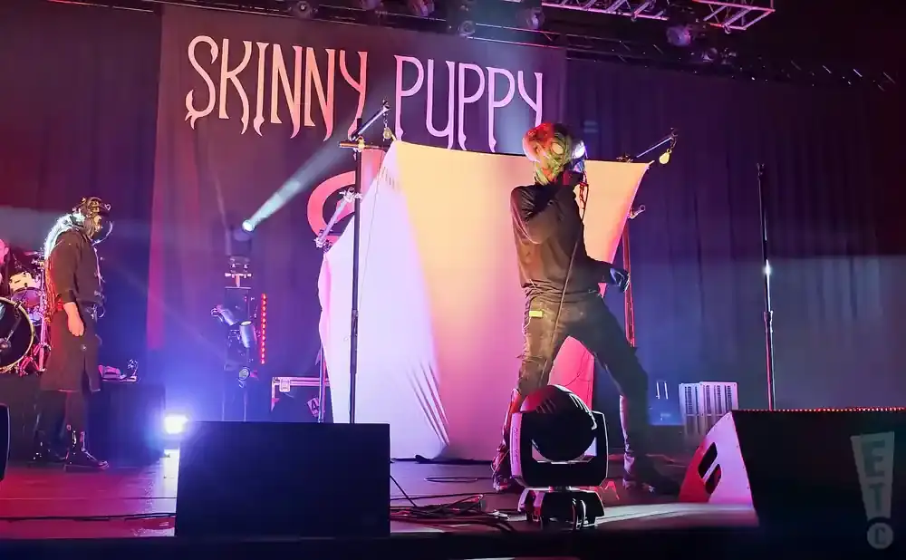 Skinny Puppy band logo behind performers on a dimly lit stage.