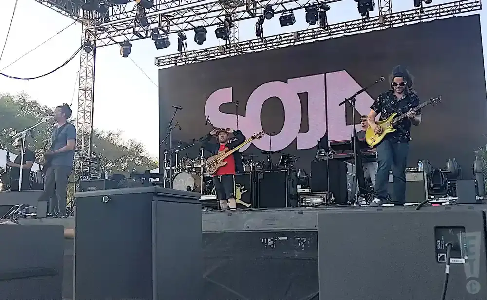 Band performing on stage with a large screen displaying 