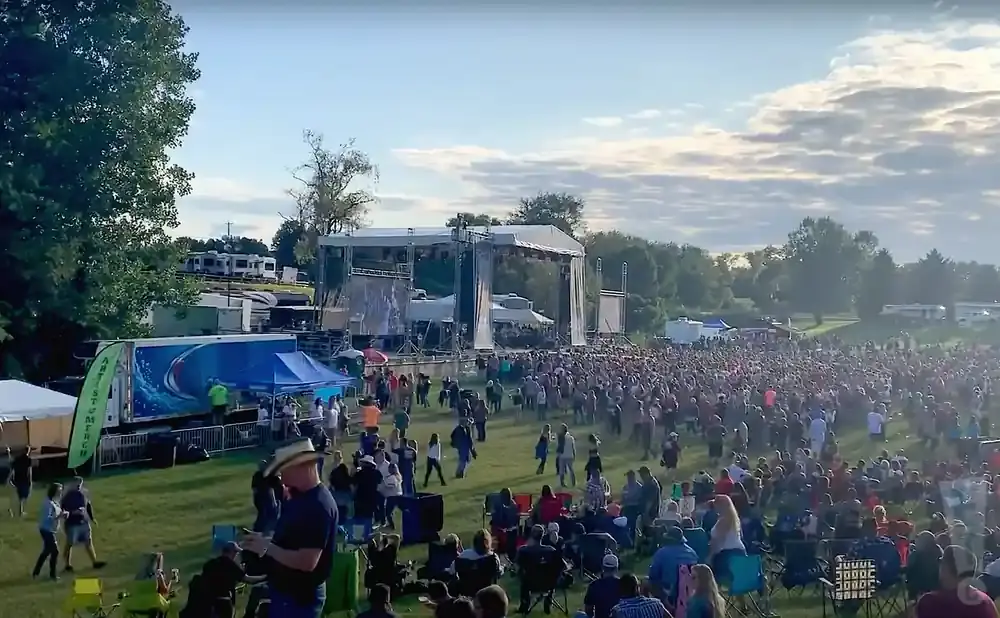 An outdoor concert with a large crowd gathered in front of a stage.