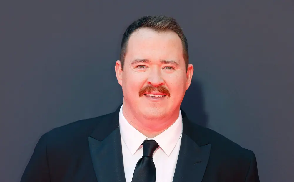 A man in a tuxedo with a mustache smiles at the camera.