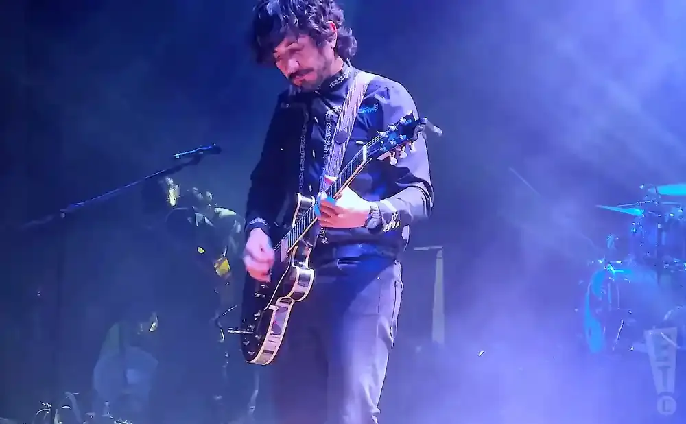 A guitarist plays on a dimly lit stage with blue stage lights.