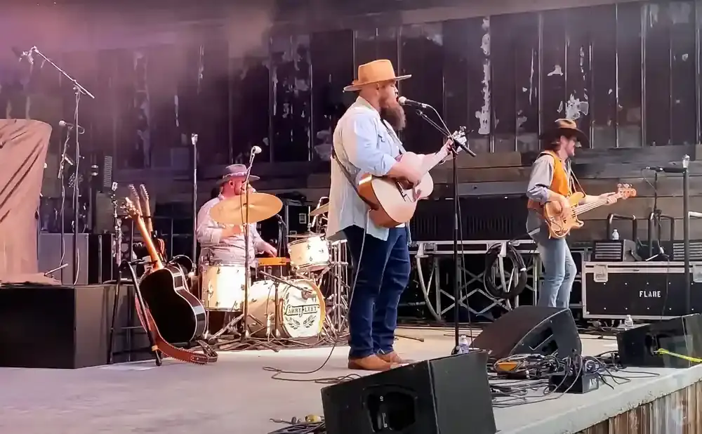 A band performs on stage, with a guitarist singing, a drummer playing, and a bassist.
