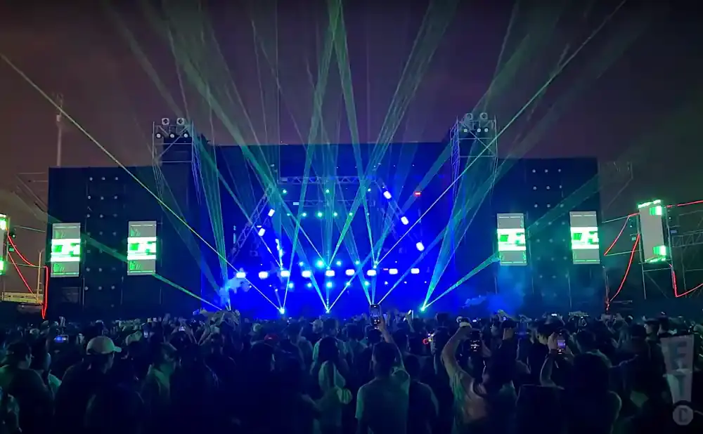 A crowd enjoys a concert with a stage bathed in blue and green lasers.