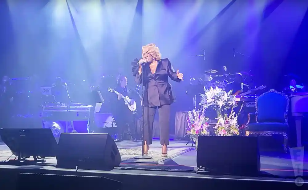 Patti LaBelle performs on stage with her band in a blue-lit venue.