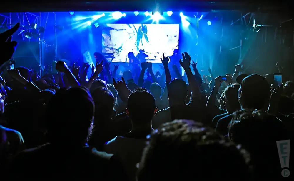Crowd at a concert with blue stage lighting and a band on screen.