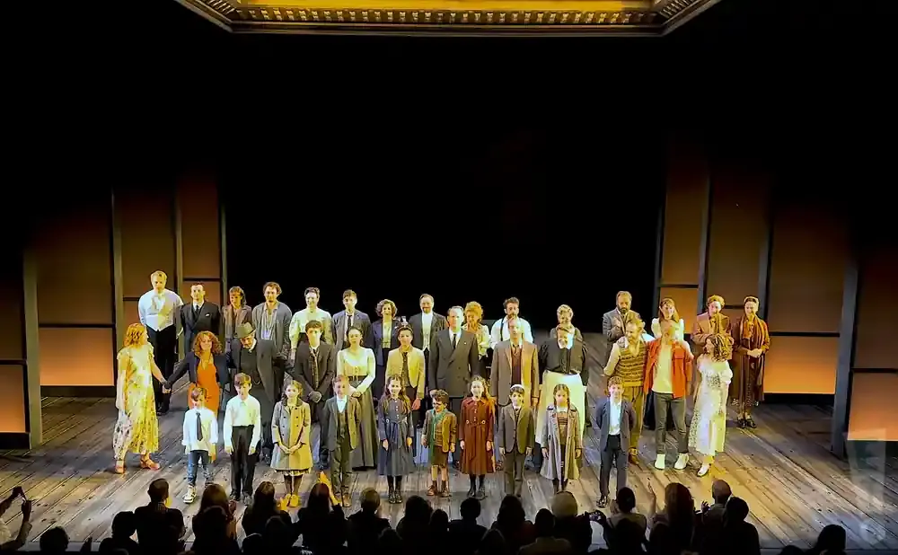 A large cast of actors, including children, stand on stage for a bow.