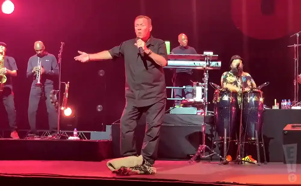 A band performs on stage with a lead singer in a black shirt holding a microphone and gesturing.