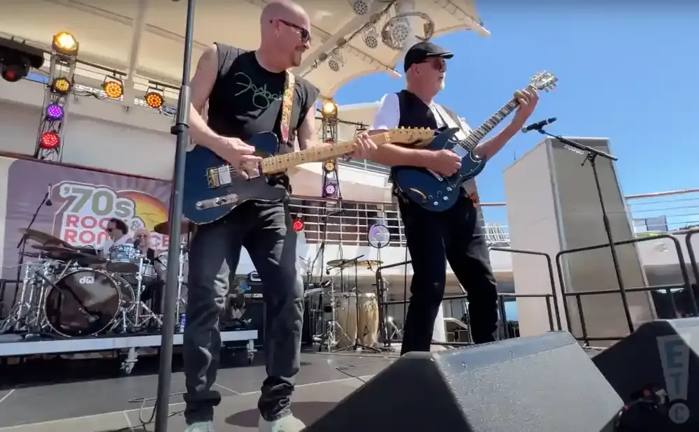 Two men play guitars on a stage with a 