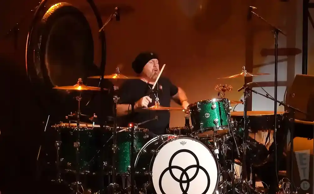 Drummer with black beanie plays a sparkly green drum kit on stage.