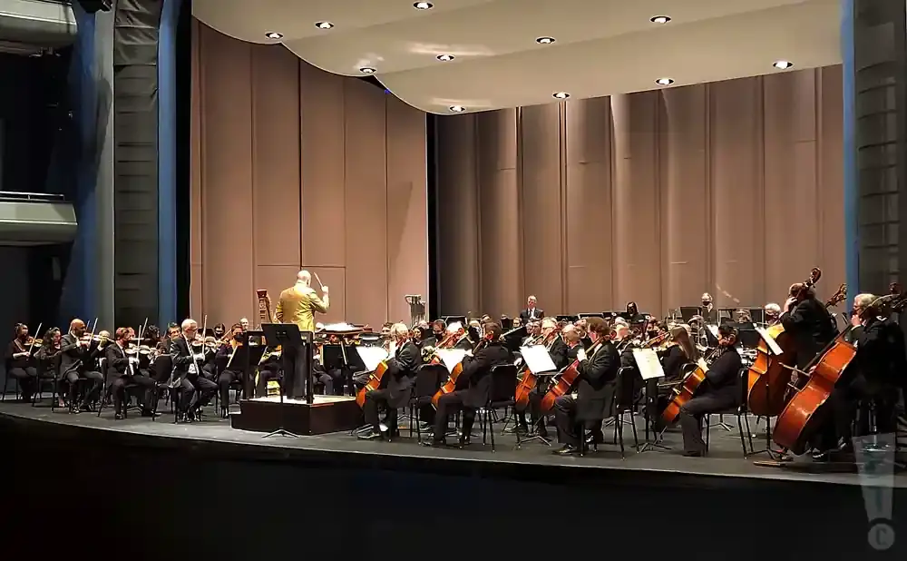 Orchestra performing on stage with a conductor leading them.