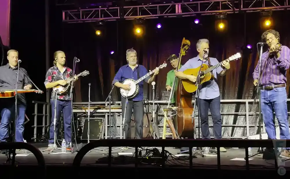 Band performs bluegrass music on stage with various instruments including guitar, banjo, mandolin, and bass.