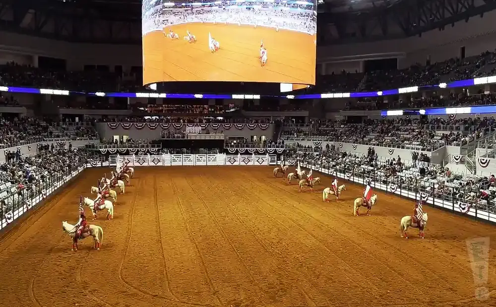 Riders on horseback with flags parade in an arena before a large crowd.