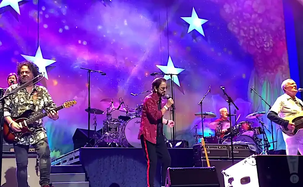A band performs on stage with a colorful, star-filled backdrop.