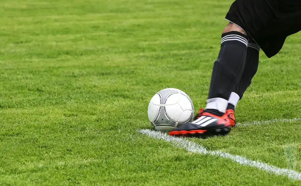 Soccer player's leg and foot about to kick a ball on a green field next to a white line.