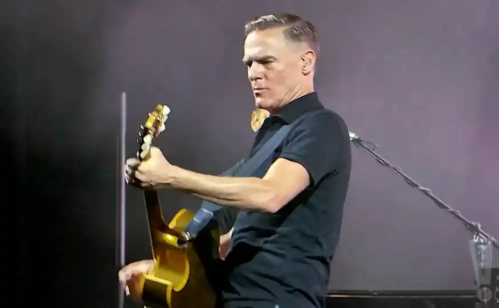 Bryan Adams on stage playing an acoustic guitar.