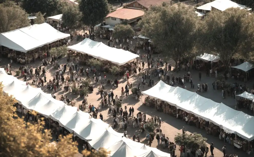 An aerial view of a bustling outdoor market with white tents and many people browsing.