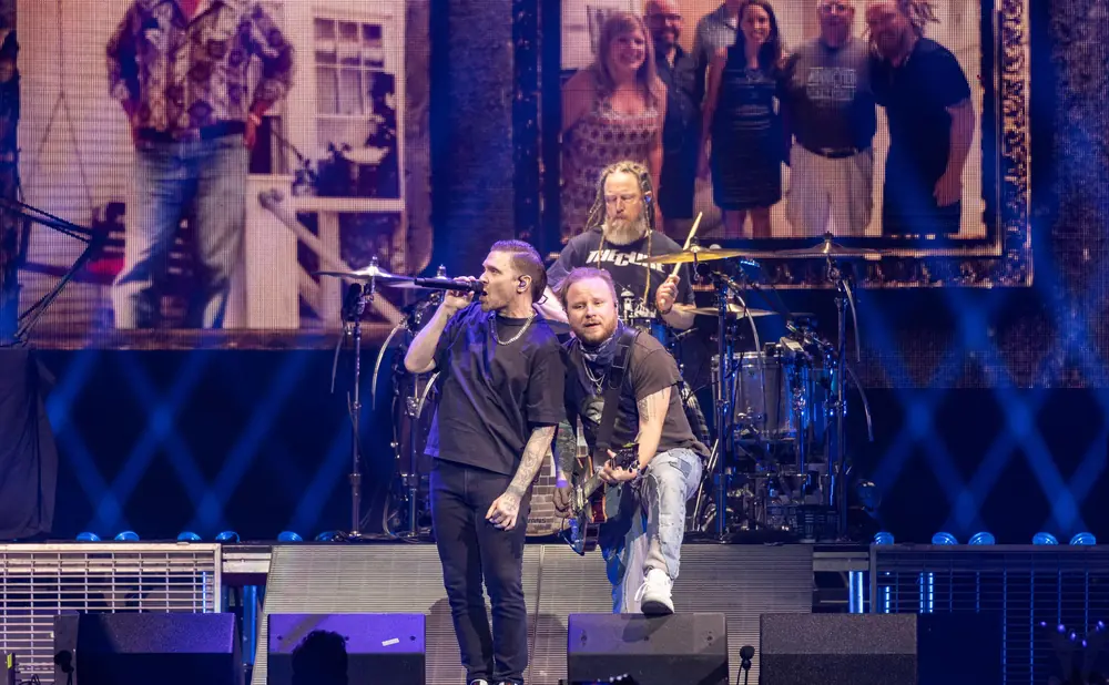 A band performs on stage with bright lights and a large screen displaying images.
