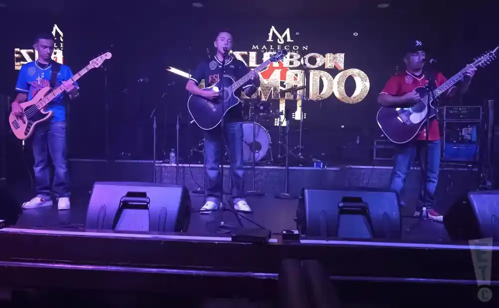 A band performs on stage with a large illuminated sign behind them that reads 