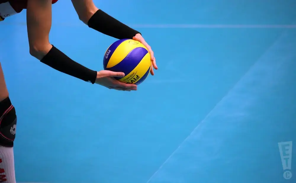 Volleyball player in black arm sleeves passes a blue and yellow FIVB ball.