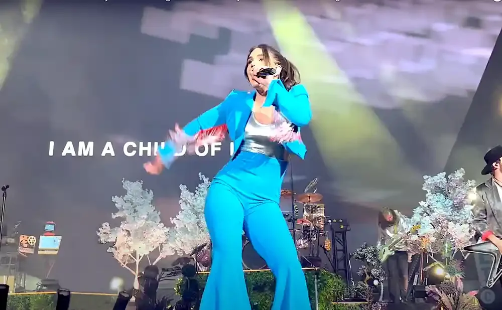 Singer performs on stage in a bright blue pantsuit, with the words 