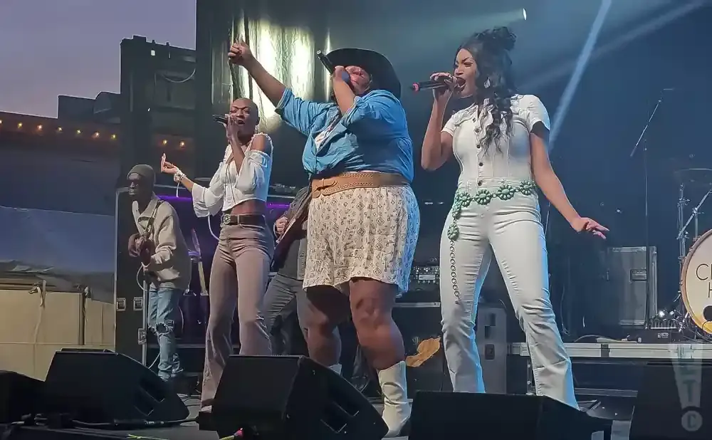 A band performs on stage with three singers and a guitarist.