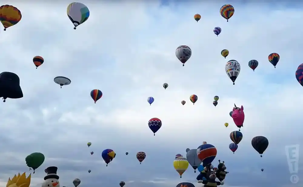 A multitude of colorful hot air balloons fill a cloudy sky, some with unique designs like a unicorn and a snowman.