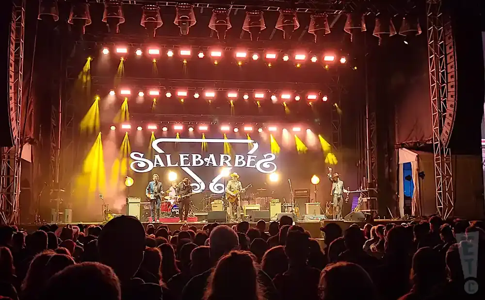 A live band performs on a stage with bright lights and a large 