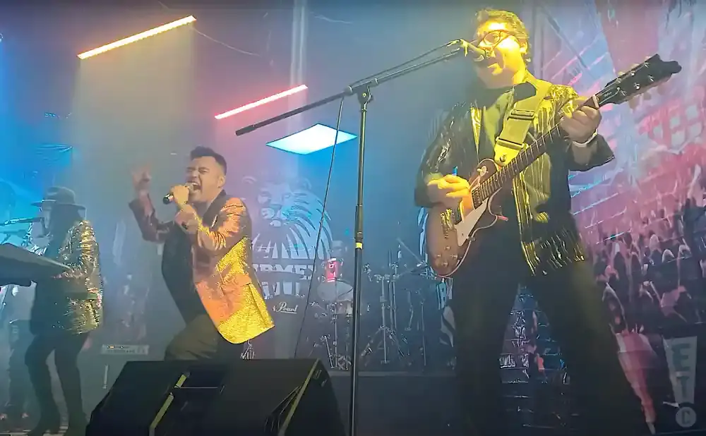 A band performs on stage with bright lights, fog, and a colorful backdrop.