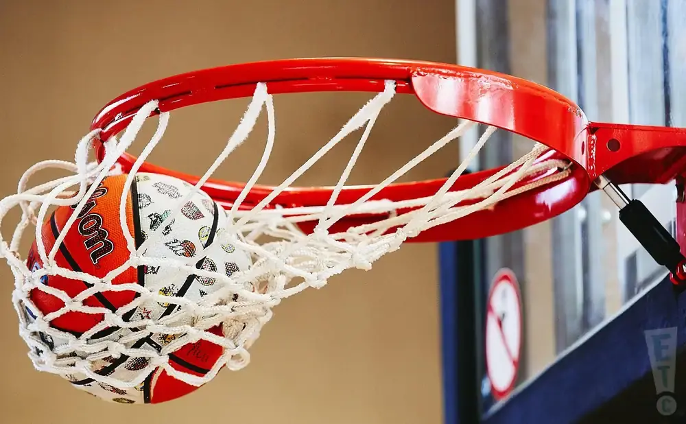 A basketball with a Wilson logo and a playful pattern is caught in a red basketball net.