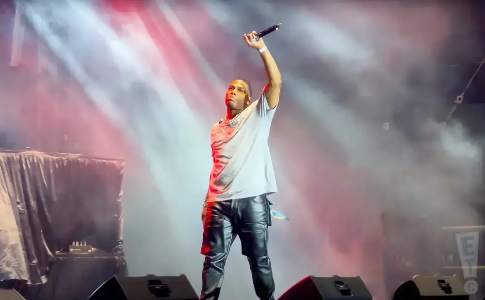 Rapper Lil Baby performs on stage holding a microphone with his arm raised.