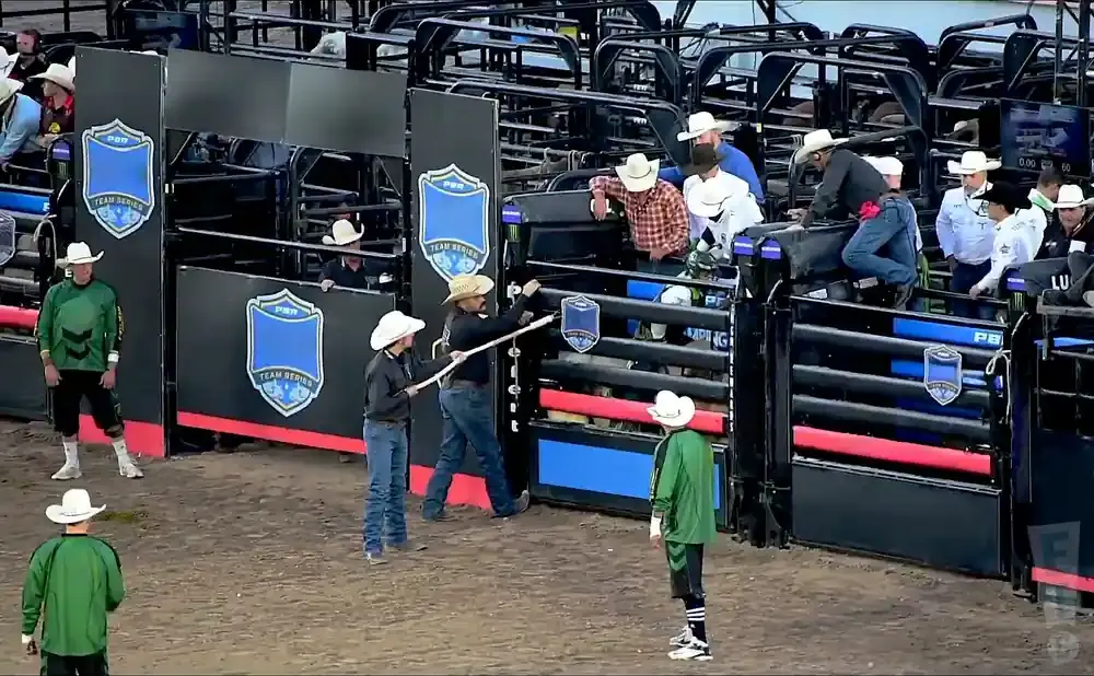Rodeo clowns and bull riders prepare in a bull riding arena.