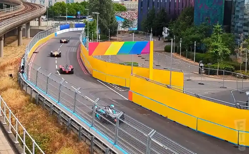 Race cars on a track with yellow barriers and a rainbow banner.