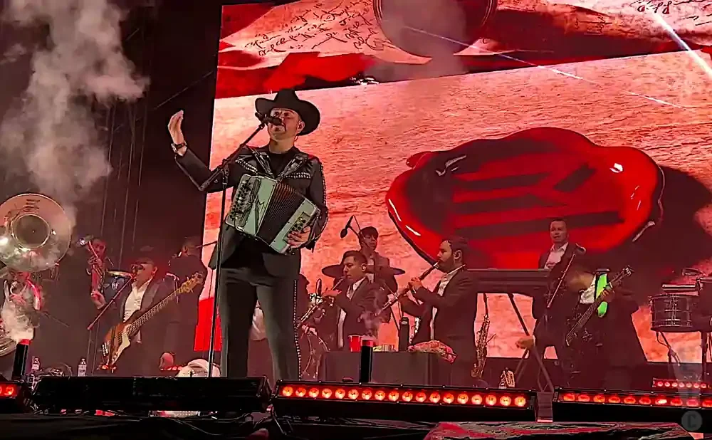 A band performs on stage with a singer in the foreground playing an accordion, under a large red heart graphic.