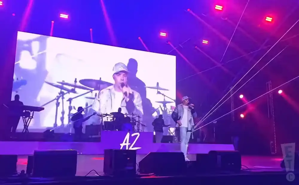 A male performer sings on stage with a large screen behind him showing a close-up of him.